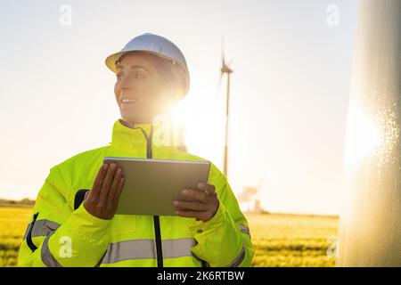 Junge Ingenieurin mit Tablet-Blick und Überprüfung von Windenergieanlagen auf dem Feld Stockfoto