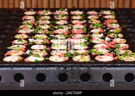 Japanisches Street Food Takoyaki in einer speziellen Grillpfanne. Prozess der Zubereitung von Takoyaki-Kugeln mit Tintenfischfüllung. Japanische Snacks und Street Food im fes Stockfoto