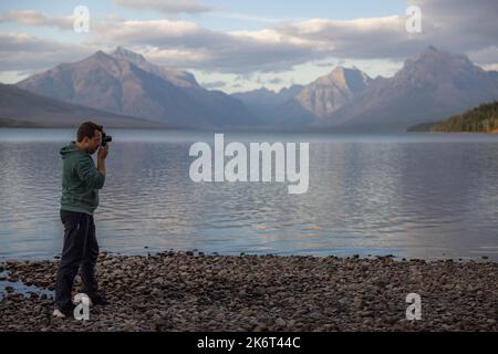 Mann, der am Ufer steht und die atemberaubenden Berge über dem McDonald-See im Glacier National Park betrachtet Stockfoto