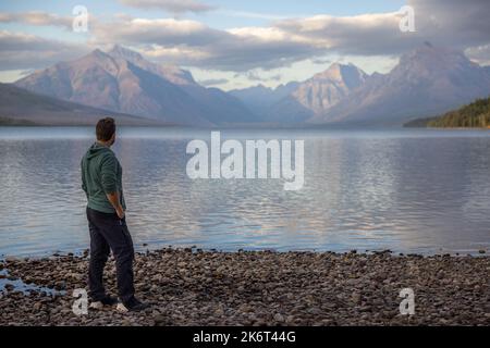 Mann, der am Ufer steht und die atemberaubenden Berge über dem McDonald-See im Glacier National Park betrachtet Stockfoto