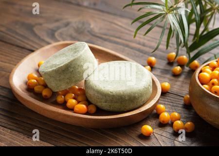 Feste Shampoo-Stücke mit Sanddornbeeren-Extrakt oder hausgemachte Bio-Seifenstücke auf Holzseifenschale. Holzschale mit Sanddornbeeren. Stockfoto