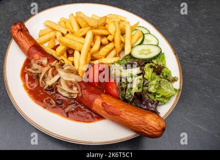 Frittierte Currywurst mit Pommes Frites, Salat und gebratenen Zwiebeln Stockfoto