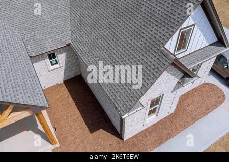 Das Dach des neu gebauten Hauses wird während der Bauarbeiten mit Asphaltschindeln bedeckt, während das Haus noch gebaut wird Stockfoto