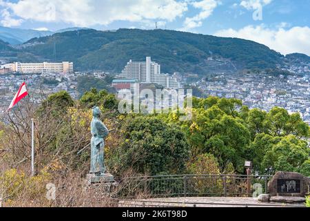 nagasaki, kyushu - 14 2021. dezember: Statue des Samurai Sakamoto Ryōma neben seiner Kaientai Reederei Flagge Betrachtung der Hügel von Nagasaki Stockfoto