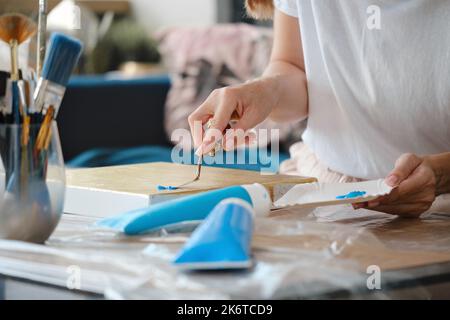 Malerhand mit Spachtel, Nahaufnahme mit Acrylfarben auf Leinwand. Künstler arbeitet im Studio. Nahaufnahme. Blaue Farben in Tuben, Bürsten. Hobby Stockfoto