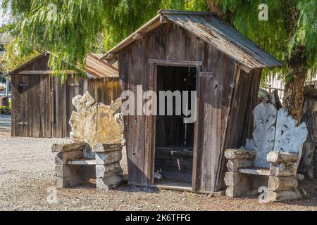 Ein altes hölzernes, schieferes Nebengebäude mit zwei ungewöhnlichen handgefertigten Stühlen auf beiden Seiten der Außenseite der Struktur in Los Alamos, Kalifornien. Stockfoto