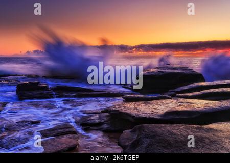 Starke Wellen des pazifischen Ozeans treffen Sandsteinfelsen von Sydney Northern Beaches am Whale Beach - dunkle Sonnenaufgangszeit. Stockfoto