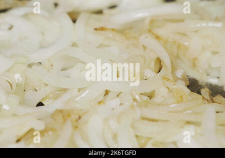 Gehackte Zwiebeln werden in einer Pfanne in Pflanzenöl gebraten und gelegentlich umrühren. Nahaufnahme. Stockfoto