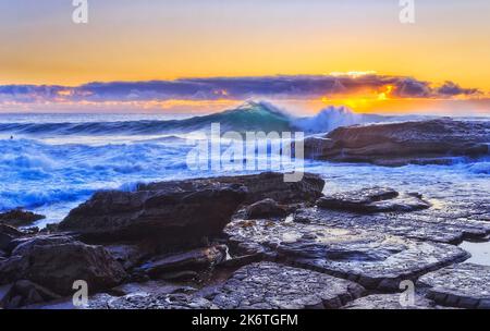 Rollende, spritzende Wellen treffen bei Sonnenaufgang auf Sandsteinfelsen am Whale Beach der Pazifikküste von Sydney. Stockfoto