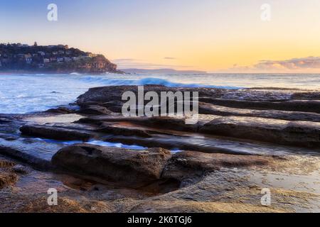 Erodierte Sandsteinfelsen am Whale Beach der Pazifikküste von Sydney, mit Blick auf den kleinen, waldigen Vorort der Northern Beaches. Stockfoto