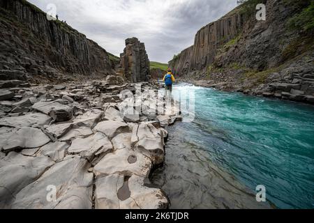 Tourist steht am Fluss im Stuolagil Canyon, türkisblauer Fluss zwischen Basaltsäulen, Egilsstadir, Island Stockfoto