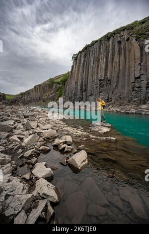 Tourist steht am Fluss im Stuolagil Canyon, türkisblauer Fluss zwischen Basaltsäulen, Egilsstadir, Island Stockfoto