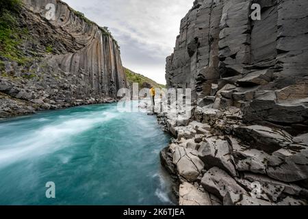 Tourist steht am Fluss im Stuolagil Canyon, türkisblauer Fluss zwischen Basaltsäulen, Egilsstadir, Island Stockfoto