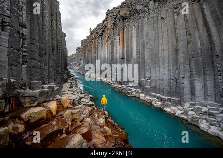 Tourist steht am Fluss im Stuolagil Canyon, türkisblauer Fluss zwischen Basaltsäulen, Egilsstadir, Island Stockfoto