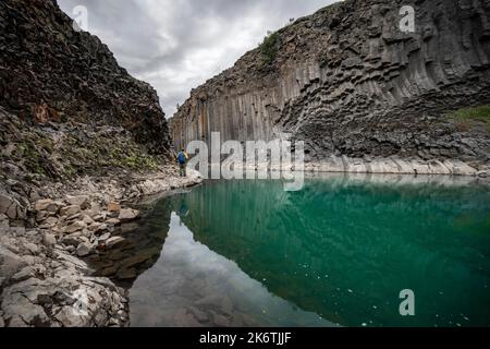 Tourist steht am Fluss im Stuolagil Canyon, türkisblauer Fluss zwischen Basaltsäulen, Egilsstadir, Island Stockfoto