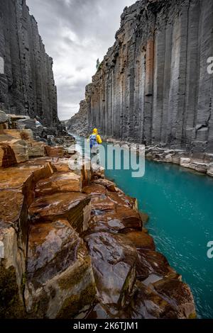 Tourist steht am Fluss im Stuolagil Canyon, türkisblauer Fluss zwischen Basaltsäulen, Egilsstadir, Island Stockfoto