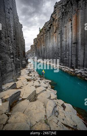 Tourist steht am Fluss im Stuolagil Canyon, türkisblauer Fluss zwischen Basaltsäulen, Egilsstadir, Island Stockfoto