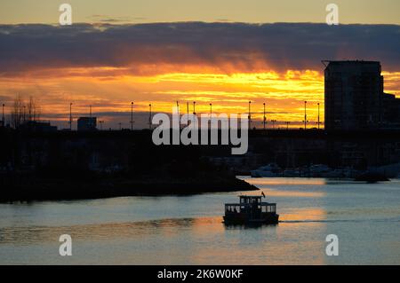 False Creek Commuter Ferry bei Sonnenuntergang. Eine Pendlerfähre überquert False Creek bei Sonnenuntergang. Stockfoto