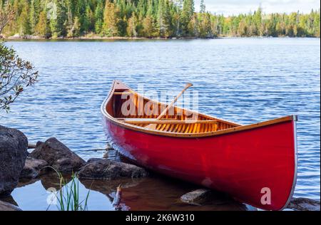 Rotes Holzkanu am Ufer eines Boundary Waters Sees an einem hellen Herbsttag Stockfoto
