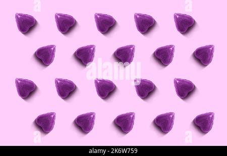 Ein sich wiederholendes Muster von herzförmigen Bonbons, die in violette Folie auf einem helleren Hintergrund eingewickelt sind. Stockfoto