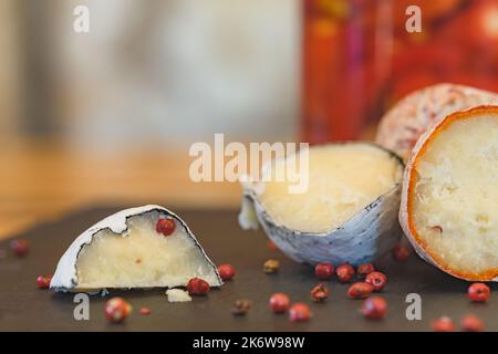 Eine Nahaufnahme von handgefertigten belper Knoblauchkugeln mit Knoblauch und rosa Pfeffer in Holzasche. Schweizer Käse. Milchig fermentierter Käse. SDOF Stockfoto