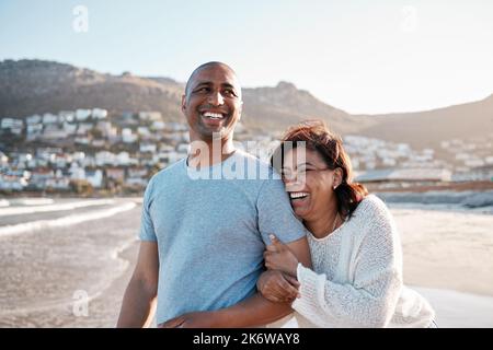 Lacht so laut, wie ihr liebt. Ein fröhliches Paar, das urkomische und lustige Witze erzählt, während es auf einem romantischen Sommerurlaub am Strand spazieren geht. Halten Sie die fest Stockfoto