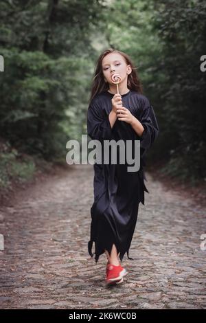 Ein süßes Mädchen in schwarzer Kleidung mit einem Bonbon auf einem Stock Stockfoto