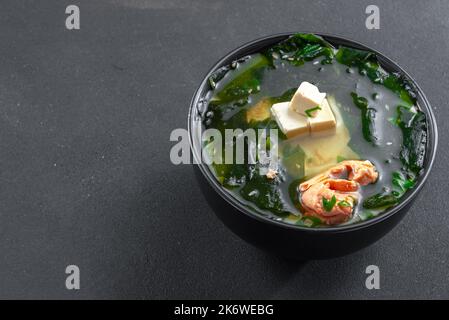 Muso-Suppe mit Lachs in einer schwarzen Schüssel auf schwarzem Hintergrund. Asiatische Küche auf dunklem Hintergrund Stockfoto