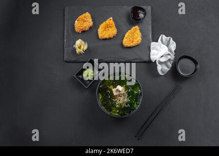 Asiatische Küche. Set aus chinesischem, thailändischem Essen auf schwarzem Hintergrund. Miso-Suppe mit Huhn und Tofu-Käse in Teig auf schwarzem Hintergrund gebraten. Satz von Stockfoto