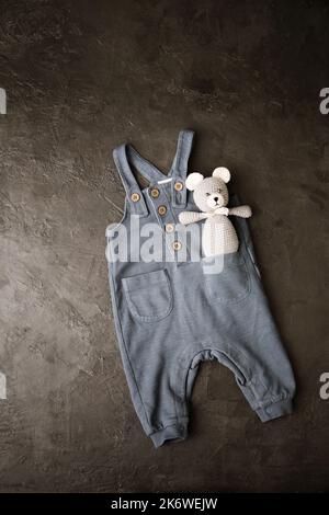 Graue Hose mit gestricktem Teddybär für ein neugeborenes Baby auf grauem Hintergrund Stockfoto