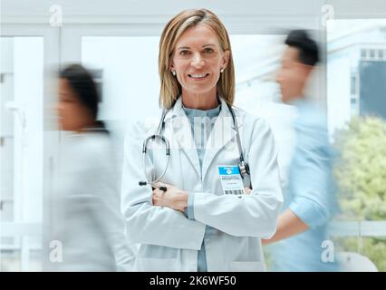 Kommt und seht mich. Eine reife Ärztin, die mit gekreuzten Armen steht. Stockfoto