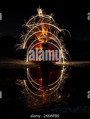Frau posiert für Lichtmalerei Fotos mit hellen Lichtern in der Dunkelheit. Reflexion im Wasser Stockfoto