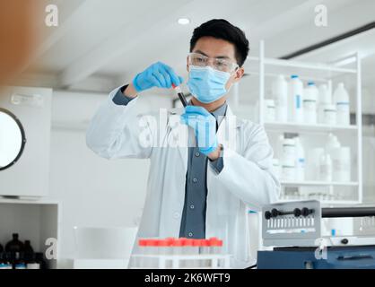 Er ist in seinem Element. Ein junger Wissenschaftler, der ein Reagenzglas füllte. Stockfoto