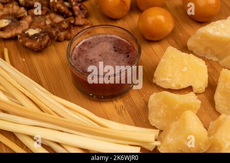 Verschiedene Sorten von Käse, Walnusskernen, geräucherten Wachteleiern und Honig in einer Glasvase auf einer Holzoberfläche. Stockfoto