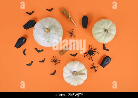 Halloween Arrangement mit weißen Kürbissen, schwarzen Spinnen, Fledermäusen und Särgen und Hexenbesen auf orangefarbenem Hintergrund Stockfoto