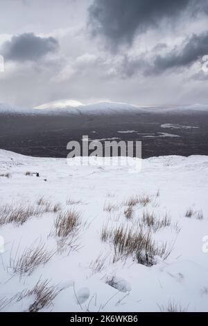 Wunderschöne Winterlandschaft von der Bergspitze in den schottischen Highlands hinunter in Richtung Rannoch Moor während Schneesturm und Spindrift von der Bergspitze hinein Stockfoto