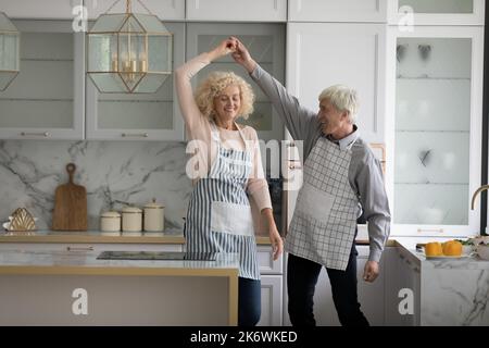 Fröhliches, lebhaftes älteres Paar, das in einer gemütlichen Küche tanzt Stockfoto