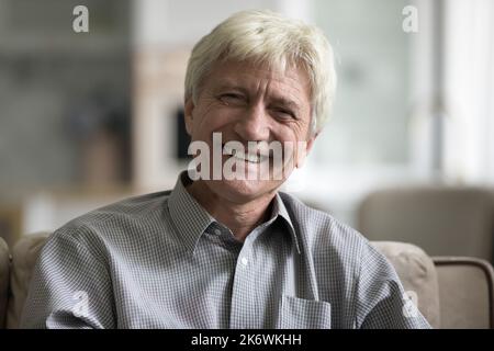 Lächelnder, gealterter Mann sitzt auf dem Sofa und starrt auf die Kamera Stockfoto