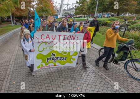London, Großbritannien. 15. Oktober 2022. Eine Gruppe von Umweltaktivisten marschiert durch einen Londoner Stadtpark mit Transparenten und Schildern, die Greenwashing anprangern. Auf einem Banner steht: „VORSICHT: Greenwash läuft #StopGreenwash“. Zu den Teilnehmern gehören ein Vortragender mit Megaphon und ein Demonstrator in einem weißen Labormantel, der wissenschaftliche Bedenken symbolisiert. Polizeipräsenz im Hintergrund sichtbar. Aktivisten von Fossil Free London veranstalten eine kleine Demonstration vor dem Londoner Hauptquartier von Shell gegen das Sponsoring von British Cycling. Penelope Barritt/Alamy Live News Stockfoto