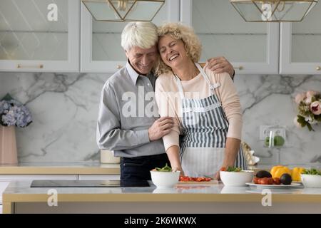Glückliches älteres Paar, das in der modernen Küche kocht und lacht Stockfoto