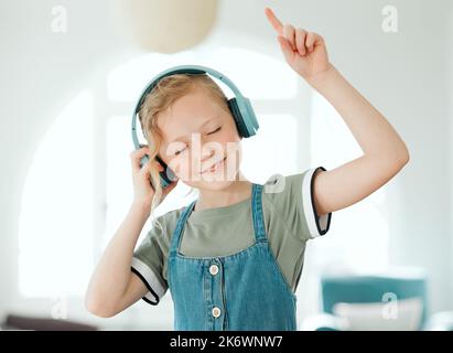 Meine neuen Kopfhörer sind unglaublich. Ein entzückendes kleines Mädchen, das allein zu Hause steht und Musik über Kopfhörer hört. Stockfoto