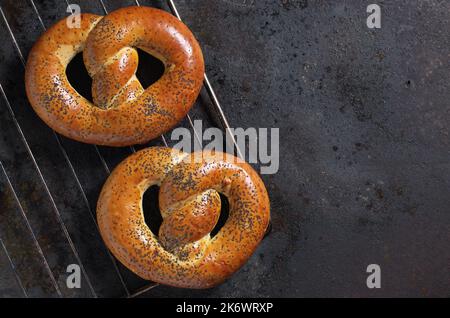 Frisch gebackene Brezeln mit Mohnsamen auf einem grüneisernen Hintergrund, Draufsicht mit Kopierfläche Stockfoto