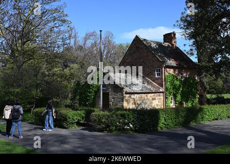 Cook's Cottage unter den Bäumen der Fitzroy Gardens, während ein Besucher vor dem historischen Wahrzeichen für ein Foto posiert Stockfoto