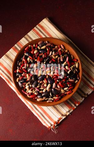 Bunte Bio-Bohnen auf burgunderrotem Hintergrund Stockfoto