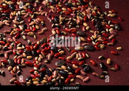 Bunte Bio-Bohnen auf burgunderrotem Hintergrund Stockfoto