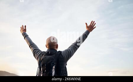 Den Berg erobern. Rückansicht eines nicht erkennbaren jungen Mannes, der die Aussicht während seiner Wanderung in den Bergen genießt. Stockfoto