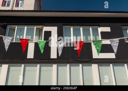 Girlande aus roten, grünen, weißen Satinfahnen, die beim Stadtfest im Wind wehen Stockfoto