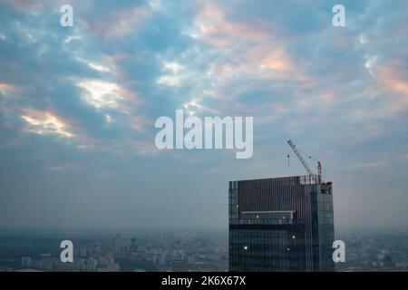 Unvollendete Wolkenkratzerkonstruktion und Turmkran gegen den dramatischen Abendhimmel Stockfoto