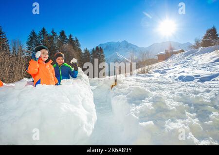 Die Brüder werfen Schneebälle in die Schneefestung, über die Berge Stockfoto