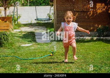 Spaß im Garten - schönes Mädchen rund um den Wasserregner laufen Stockfoto